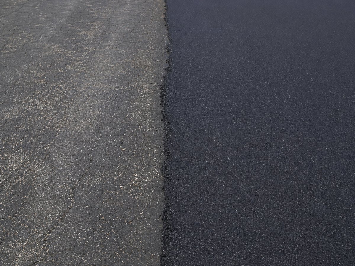 Driveway maintenance in Madison WI showing worn asphalt beside a cleaner maintained asphalt surface