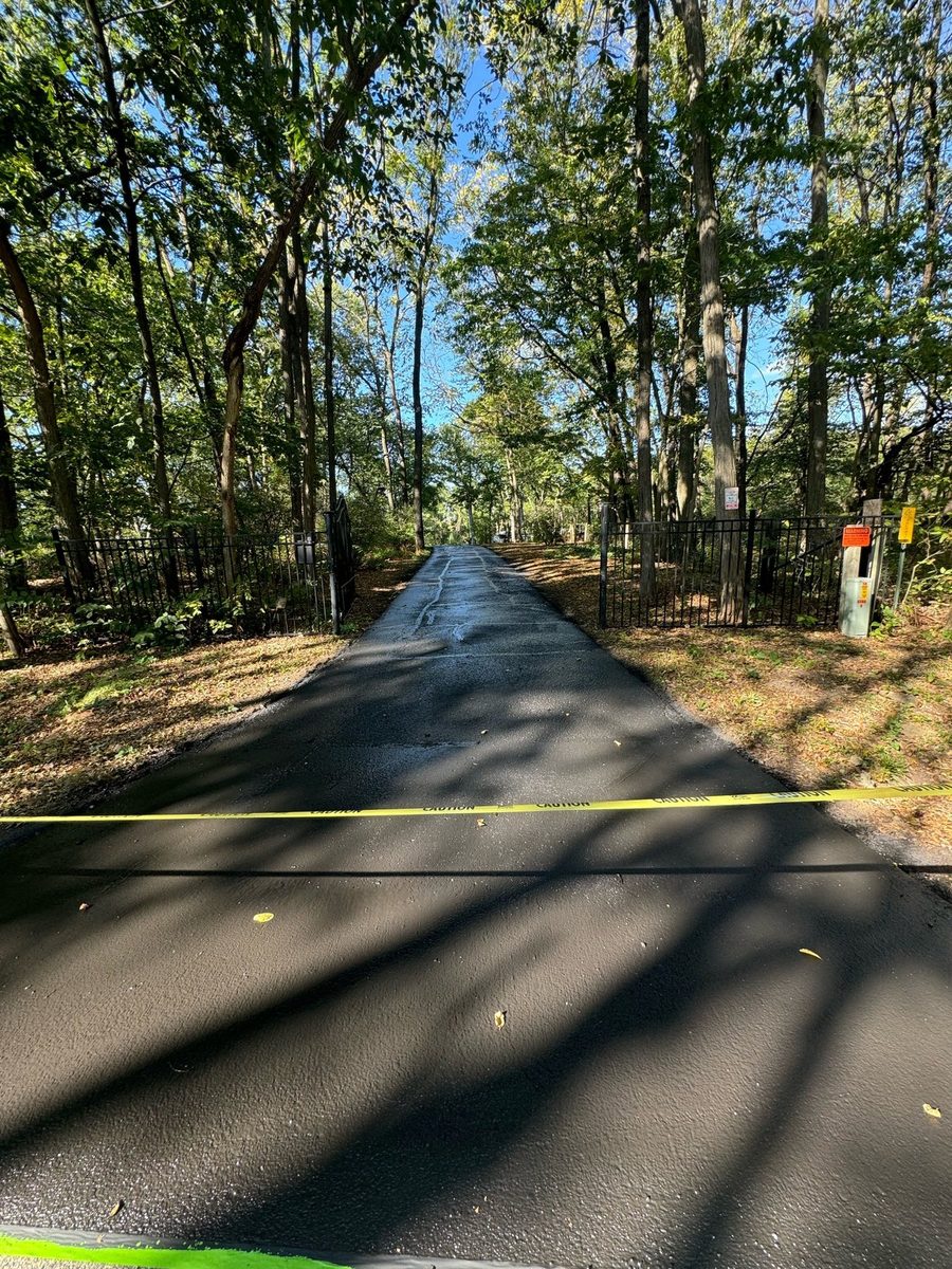Fresh dark asphalt driveway leading through a wooded gated entrance