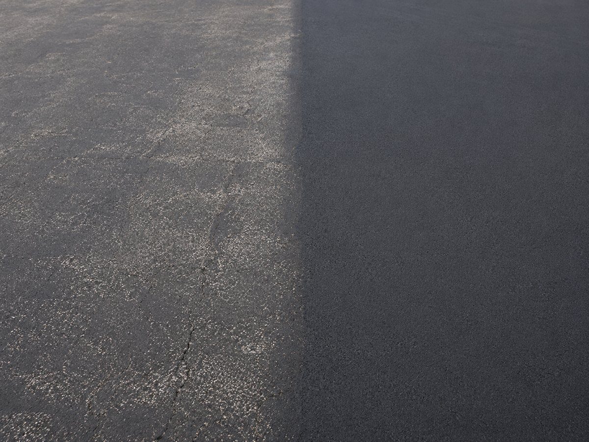 Sealcoating in Madison WI showing worn asphalt beside freshly sealed black asphalt